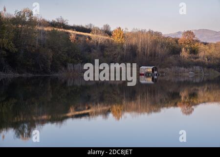 Small, colorful raft parked in a calm, silver blue, reflective lake and trees colored with autumn colors Stock Photo