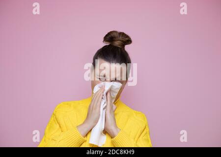 Studio portrait of unhealthy Caucasian female with paper napkin sneezing, experiences allergy symptoms, caught a cold. Sick desperate woman has flu Stock Photo