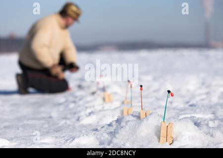 winter fishing activities. Focus on fishing nets for ice fishing, blurred fisherman checks fishing rod, sunny winter frosty day. Stock Photo