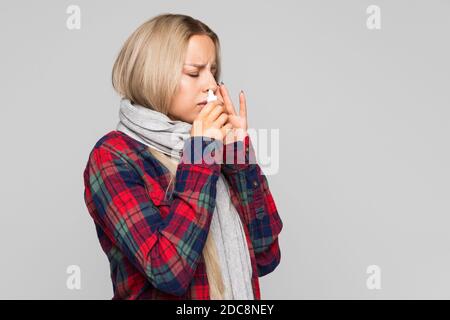 Close up Of upset woman in checked shirt wrapped in scarf using nasal spray to help herself. Seasonal health issues. Rhinitis, flu season. Stock Photo