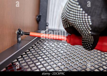 Mounting of metal flat pack furniture by handyman. Worker is assembling modern shelf using screwdriver. Stock Photo