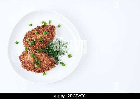 Two juicy cutlets are sprinkled with green onions and dill in a white plate on a light background. Stock Photo