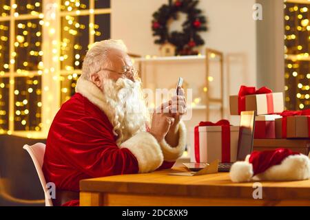 Modern Santa Claus text messaging and ordering presents delivery using phone app Stock Photo