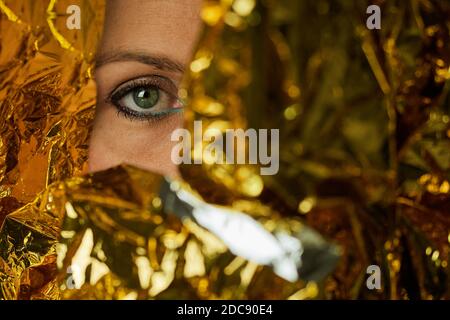 Green eye of a woman wearing makeup and wrapped in gold foil Stock Photo