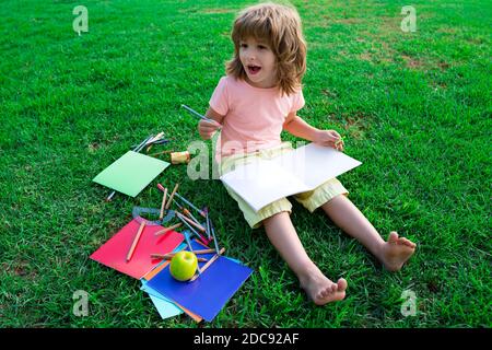 Kids Exam Study. Funny little student boy reading book outdoors, lying on lawn in park, studying at School backyard. Stock Photo