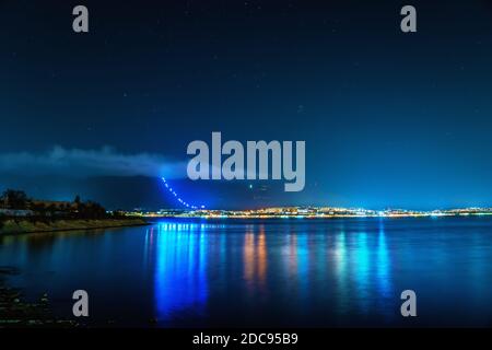 Small resort city Gelendzhik with mountains and night illumination reflected in sea bay water and bright night sky with stars. Gelendzhik - big letters on mountains on Russian language Stock Photo