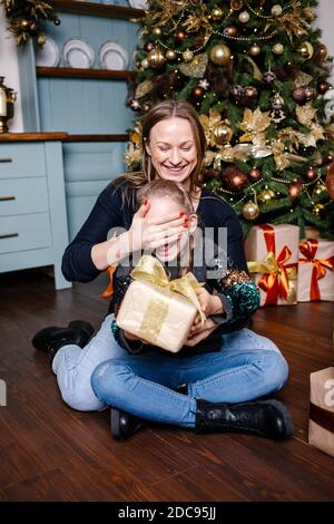 https://l450v.alamy.com/450v/2dc95jj/mother-covers-her-daughters-eyes-and-going-to-make-surprise-for-daughter-gives-present-near-christmas-tree-at-home-happy-smiling-girl-receives-gift-2dc95jj.jpg