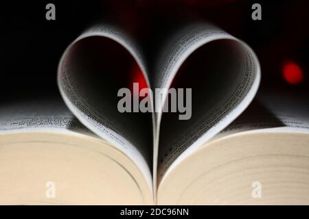 Pages of a book curved into a heart shape with dark background and red lights and bokeh Stock Photo