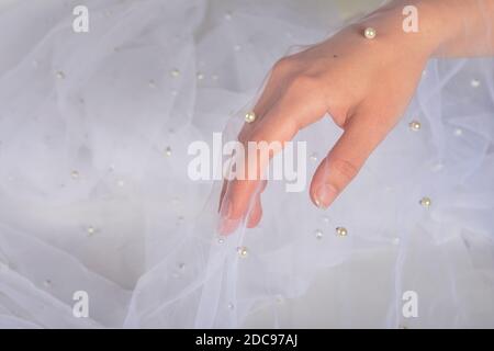 elegant women's hand with white elastic fatin fabric organza tulle mesh with pearl beads. for sewing wedding and masquerade dresses. space for text. Stock Photo