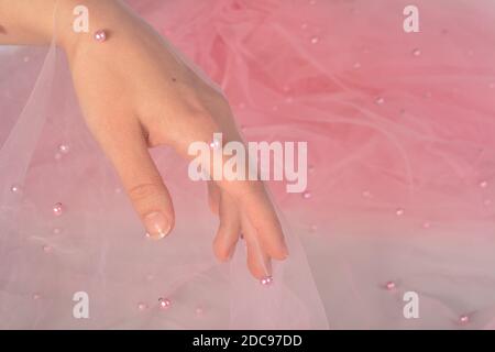 elegant women's hand with pink elastic fatin fabric organza tulle mesh with pearl beads. for sewing wedding and masquerade dresses. space for text. Stock Photo
