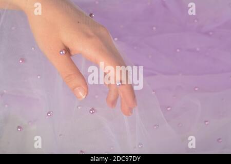elegant women's hand with purple elastic fatin fabric organza tulle mesh with pearl beads. for sewing wedding and masquerade dresses. space for text. Stock Photo