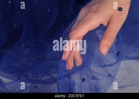 elegant women's hand with blue elastic fatin fabric organza tulle mesh with pearl beads. for sewing wedding and masquerade dresses. space for text. Stock Photo