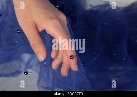 elegant women's hand with blue elastic fatin fabric organza tulle mesh with pearl beads. for sewing wedding and masquerade dresses. space for text. Stock Photo
