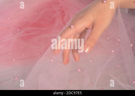 elegant women's hand with pink elastic fatin fabric organza tulle mesh with pearl beads. for sewing wedding and masquerade dresses. space for text. Stock Photo