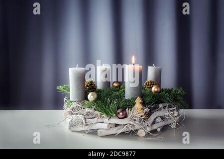 First advent with a burning candle on a wreath of white painted wood, fir branches and Christmas decoration against a purple-grey background, copy spa Stock Photo