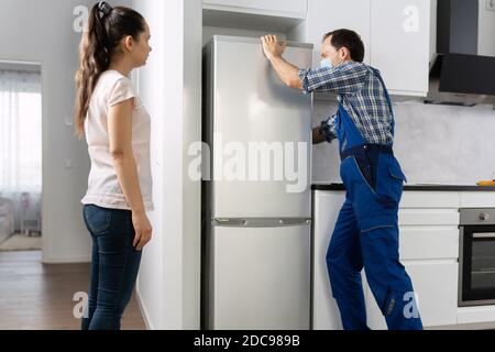 Fridge Handyman Service In Face Mask. Broken Refrigerator Stock Photo