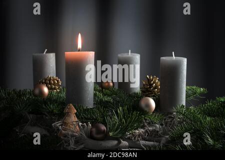 Four candles, one of them lit on an advent arrangement from fir branches and Christmas ornaments, holiday decoration against a dark gray background wi Stock Photo