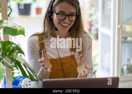 Smiling gardener millennial woman wear headphones talk in video chat, using laptop, communicating with clients, watching webinar or video stream confe Stock Photo