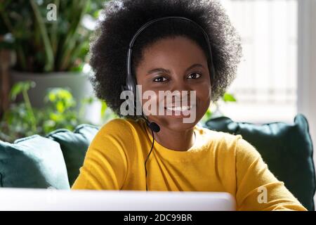 Smiling African American consultant woman wear headphones looking at camera while remote work on computer during lockdown. E-business, customer care s Stock Photo