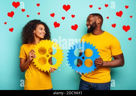 Couple with gears in hand over light blue background. Concept of meeting and love Stock Photo