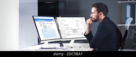 Young Businessman Looking At Invoice While Doing Online Banking On Computer Stock Photo