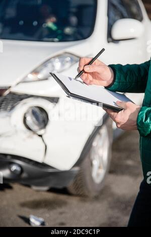 Insurance agent will examine and examine the damage to the car after an accident. Inspection of the car after an accident on the road. The front fende Stock Photo