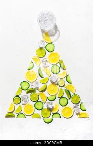 Colorful pattern made of slices of citrus fruits  lemon, lime and cucumber. Gin garnish concept as Christmas tree with ice cubes and glass of gin on w Stock Photo