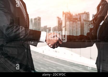 Double exposure image of business people handshake on city office building in background showing partnership success of business deal. Concept of Stock Photo