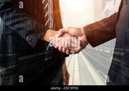 Double exposure image of business people handshake on city office building in background showing partnership success of business deal. Concept of Stock Photo