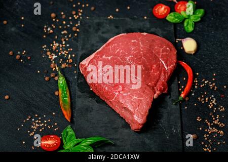 Juicy fresh beef steak. Grass-fed meat with spices and herbs on a dark background. Stock Photo