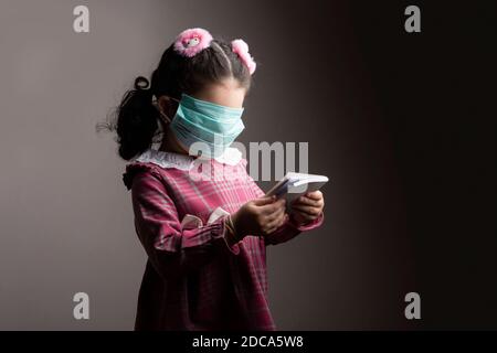 Covered face of a little girl with protection hospital mask when studying a book, Anonymity and blindness concept Stock Photo