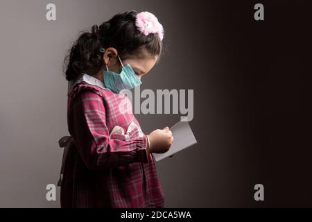 A little girl with protection hospital mask studying a book, Anonymity and virus protection concept Stock Photo