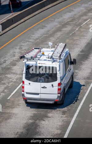 Compact commercial cargo mini van for delivery and small business services with ladders on the roof driving on the turning overpass road intersection Stock Photo