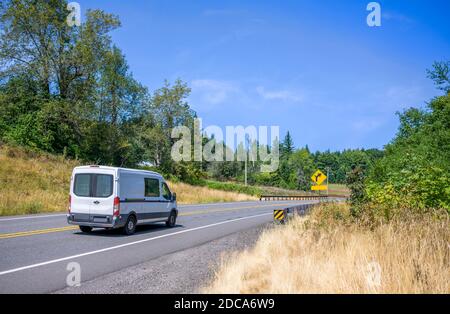 Compact white cargo mini van for small business and delivery purpose driving on the winding summer road with beautiful nature around with trees and hi Stock Photo