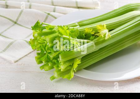 Bunch of fresh green celery stalks on a white plate over a white wood table. Natural antioxidant, healthy eating and weight loss diets ingredient. Stock Photo