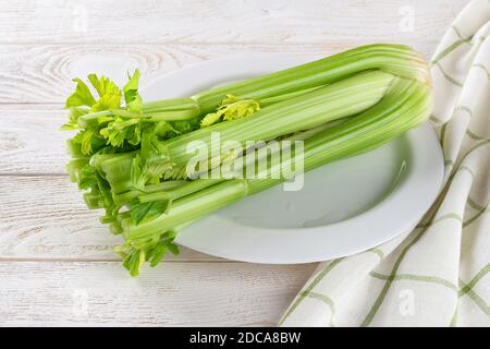 One bunch of fresh green celery stalks on a white plate over a white wood table. Natural antioxidant, healthy eating and weight loss diets ingredient. Stock Photo