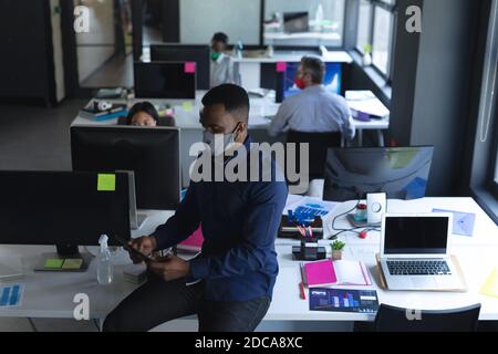 African american man wearing face mask using tablet in office Stock Photo