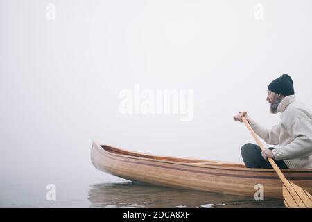 Hipster man paddling canoe on the foggy lake Stock Photo