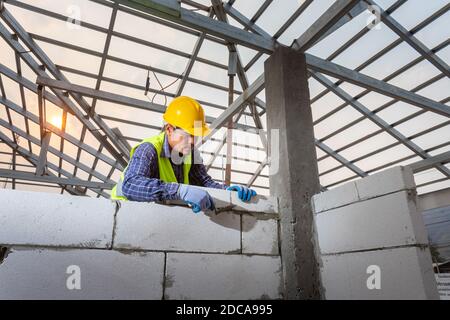 Asain worker bricklayer builder working with autoclaved aerated concrete blocks. Walling, installing bricks in construction site. Stock Photo