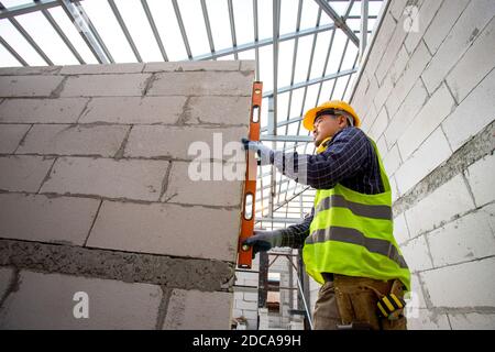 Asain worker using water level meter measuring the wall builder working with autoclaved aerated concrete blocks. Walling, installing bricks in constru Stock Photo