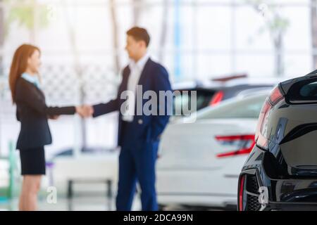 Selective focus on a new car and blur the dealership professional salesman and his client shaking hands. concept dealer Cars For Sale. Stock Photo