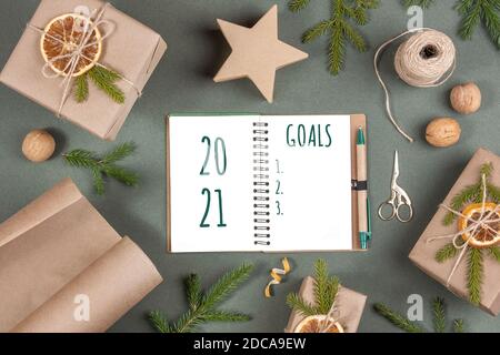 2021 Goals text on white notepad, boxes, craft paper, twine, scissors, dried oranges and natural decor on green background. Concept Merry Christmas an Stock Photo