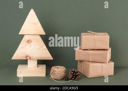 Xmas or New Year composition. Homemade wooden Christmas tree, three gifts, twine and spruce cone on green background. Concept christmas zero waste, ec Stock Photo