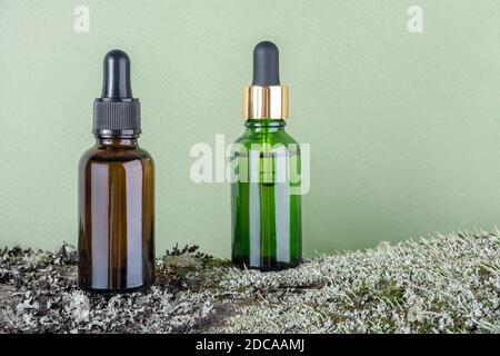 Two brown, green glass bottles with serum, essential oil or other cosmetic product on tree bark covered with moss against green background. Natural Or