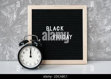 Text Black friday on black letter board and alarm clock on table against grey stone background. Concept Black friday , season sales time. Stock Photo