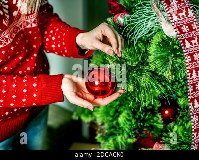 Hands of woman or girl close up decorates a Christmas tree for Christmas or New Year. She hangs wooden toys on the Christmas tree - Snowflake, star, d Stock Photo