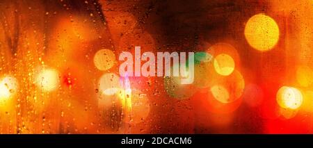 Banner of colorful city lights blurred with bokeh effect on a rainy day at night behind raindrops on a windshield Stock Photo