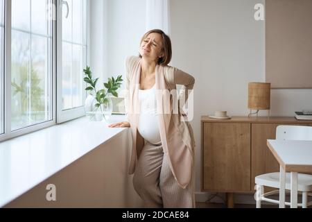 Healthcare, treatment. Young pregnant woman feeling sudden pain in her back. Future mom suffering from backpain. Stock Photo