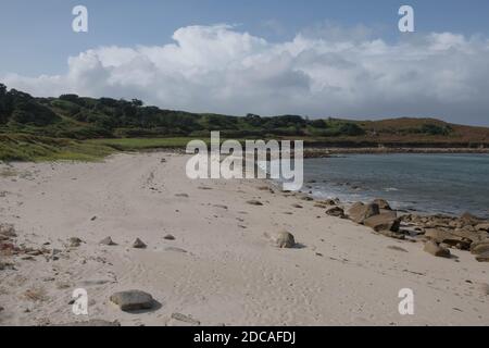 Deserted Gimble Porth Beach with Round Island Lighthouse in the Distance and Cloudy Blue Sky Background on the Island of Tresco in the Isles of Scilly Stock Photo
