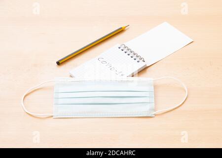 A face mask, a spiral notepad with "Covid-19" written on it and a pen are arranged on a wooden table. To-do list concept during the Covid-19 Outbreak. Stock Photo